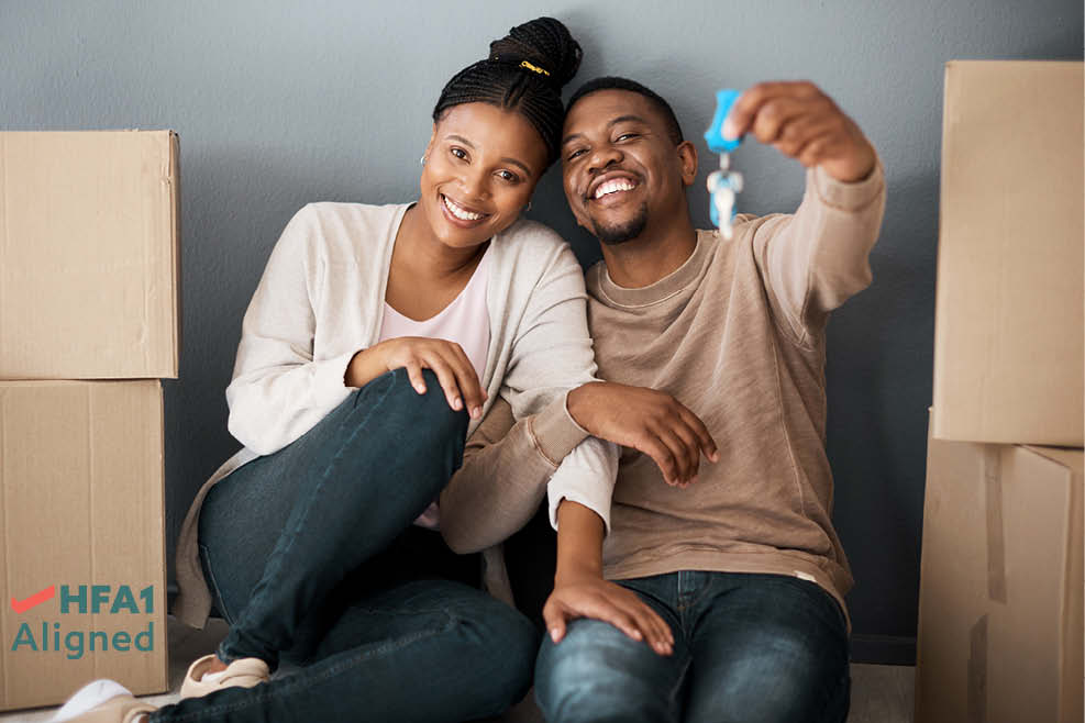 A young couple surrounded by moving boxes, holding up a key