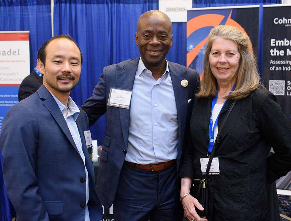 Three people in a conference exhibit hall smiling