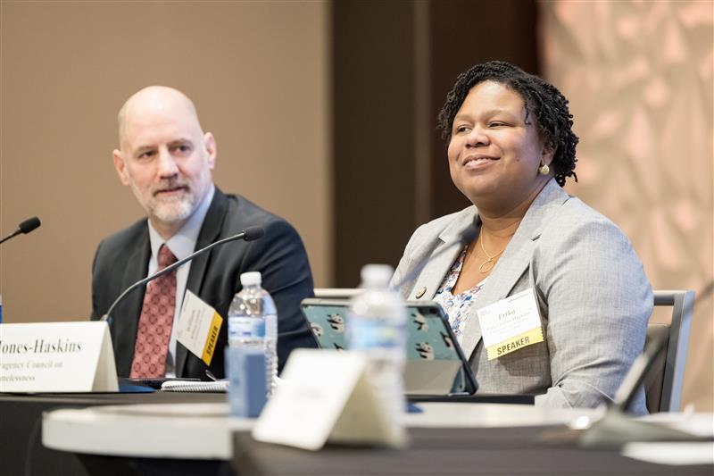 Two speakers seated at table on stage